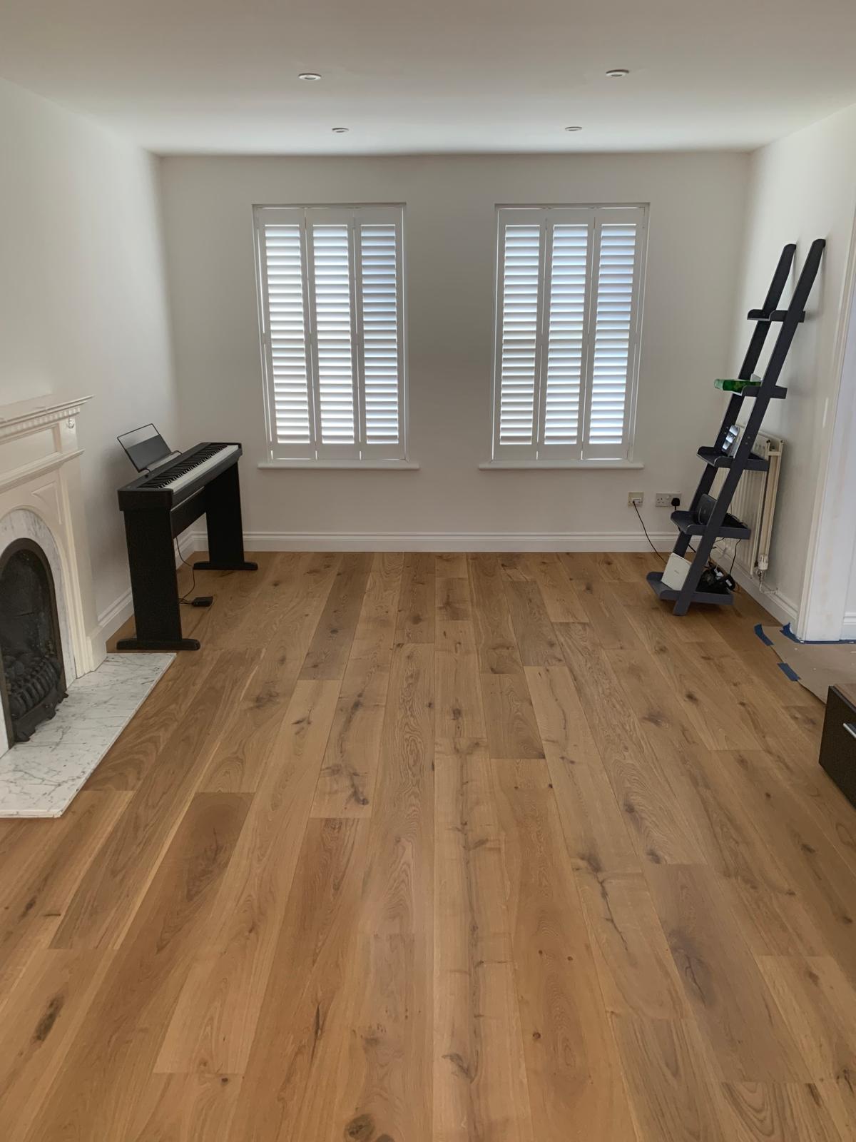 Empty living room with a wide oak floor and shuttered windows