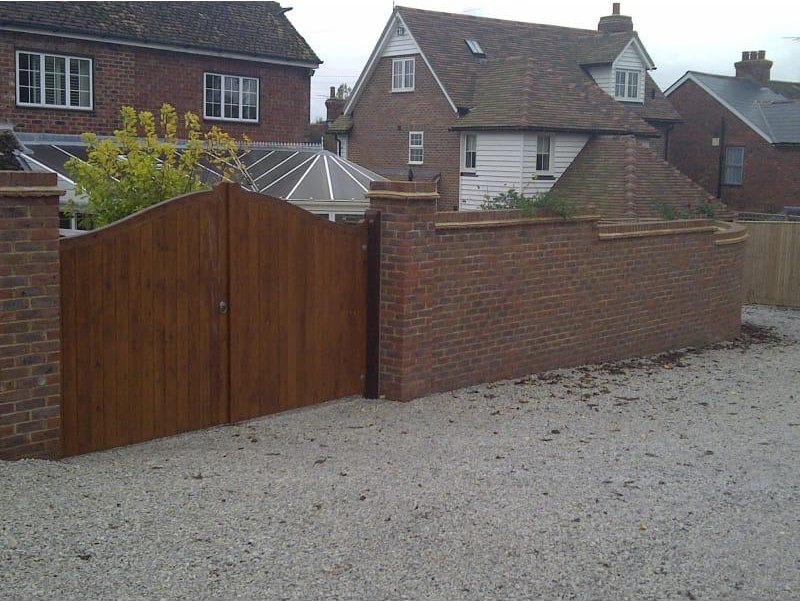 Brick boundary wall with piers and wooden gates beside a gravel driveway